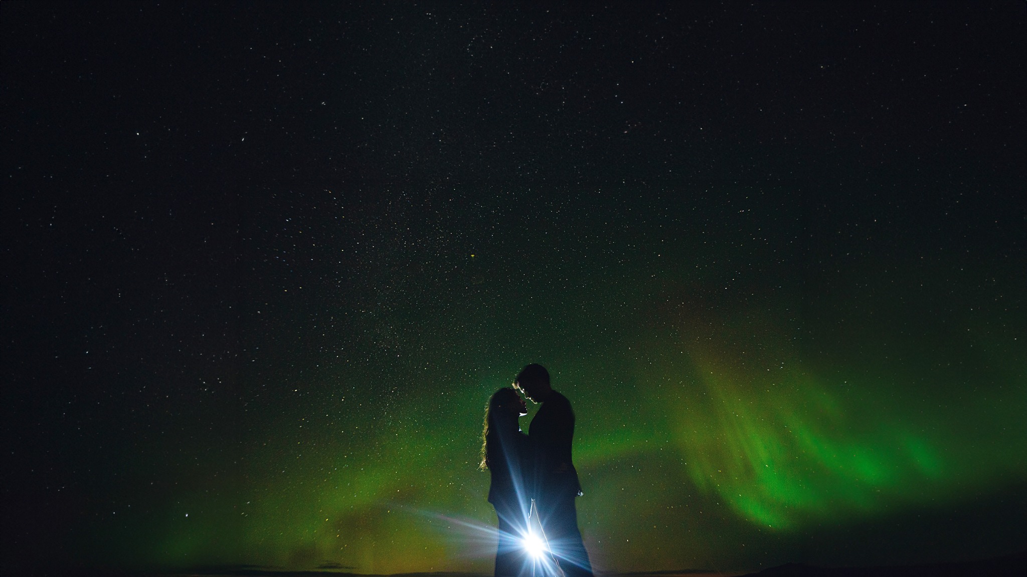 Couple silhouetted beneath the northern lights and a star-filled sky in Iceland