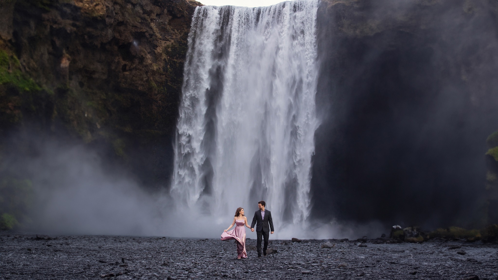 Couple walking in front of a large waterfall during a destination portrait session in Iceland
