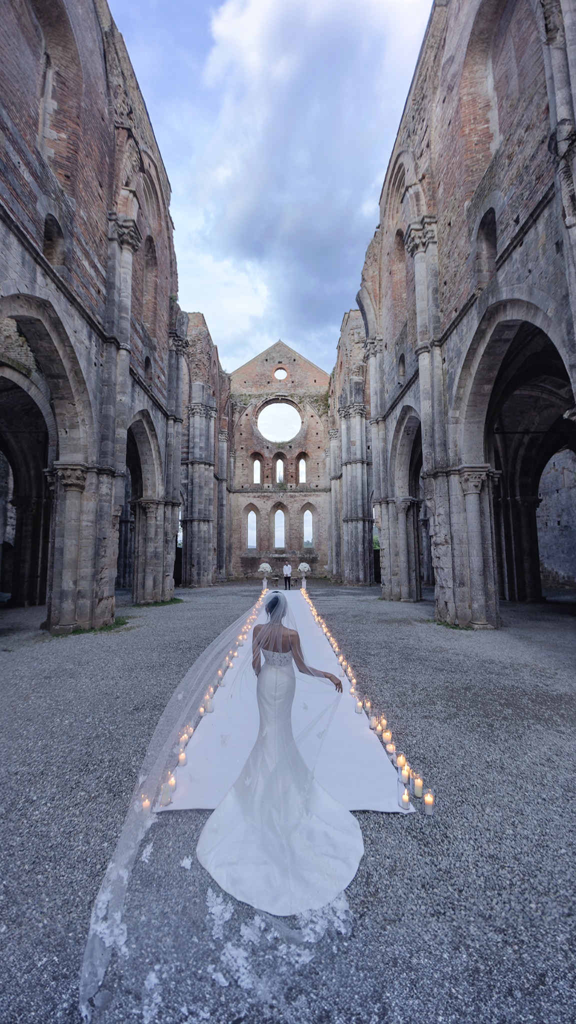 Bride walking toward an outdoor ceremony aisle inside historic stone ruins in Italy