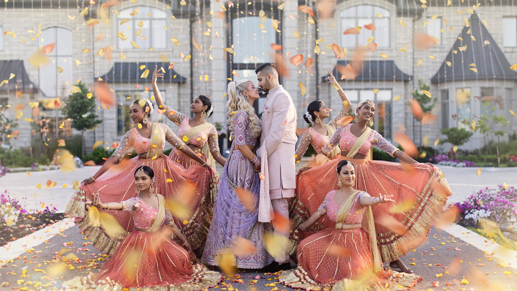 South Asian wedding couple surrounded by dancers and falling flower petals