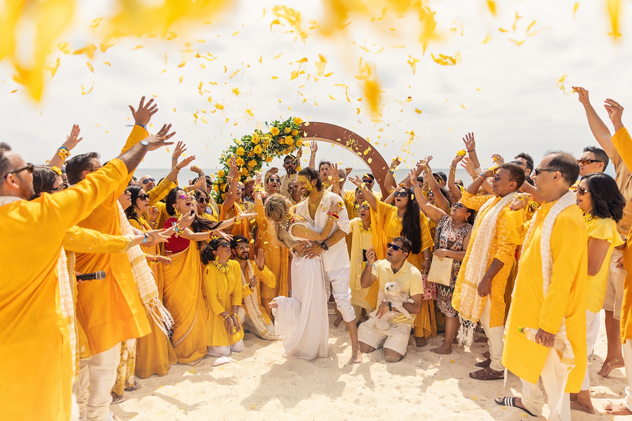 Guests in yellow attire celebrating with the couple during a South Asian beach wedding
