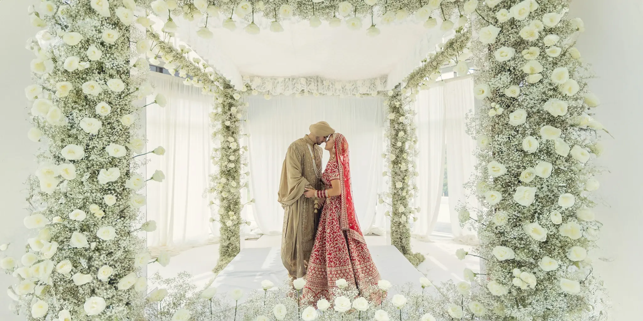 Bryanna and Raj beneath white florals during their multicultural Sikh wedding celebration